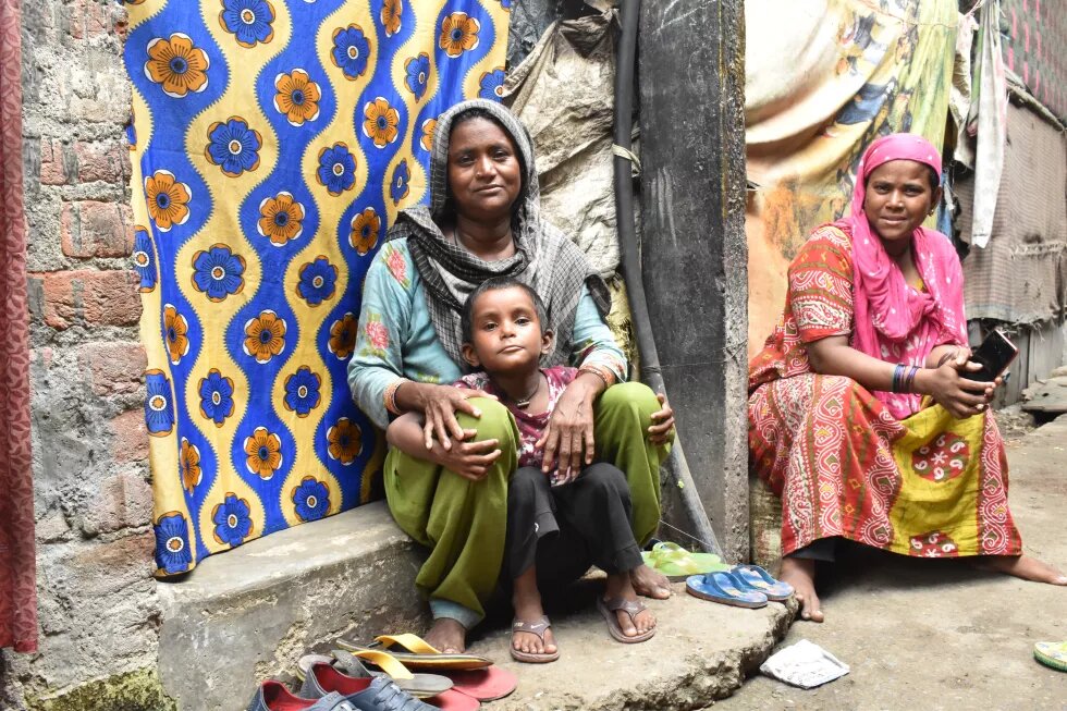 Two waste pickers sitting outside their homes, taking a quick break from their work to play with their children. 