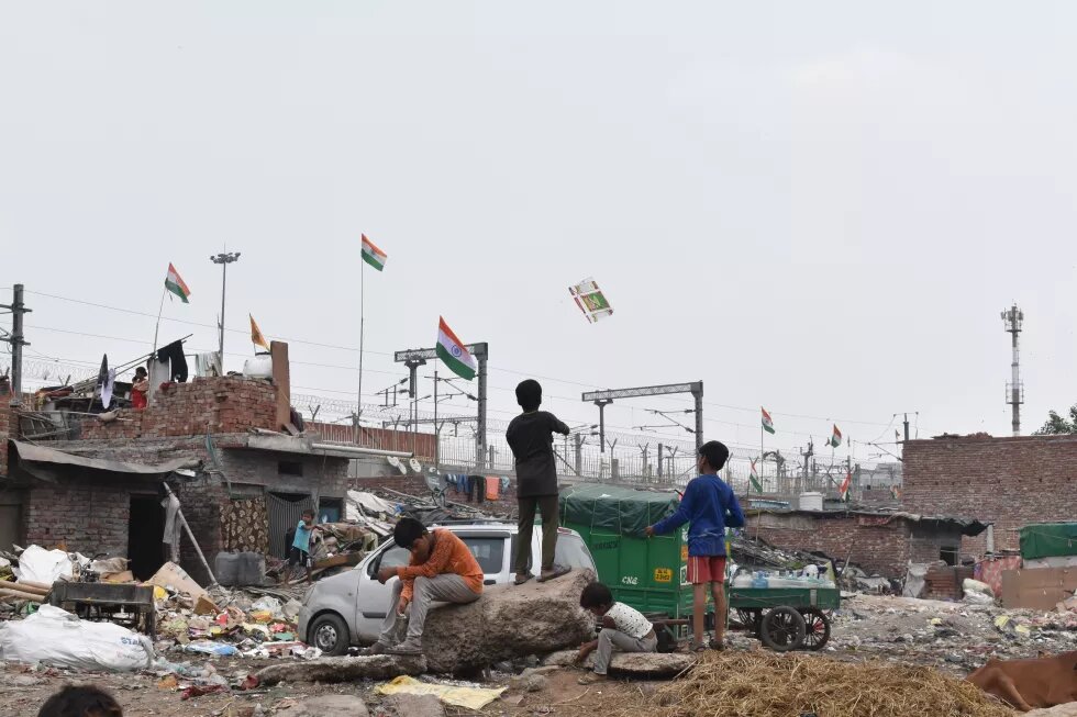 Three children sitting on a cart and playing with plastic objects they found in the garbage lying around.